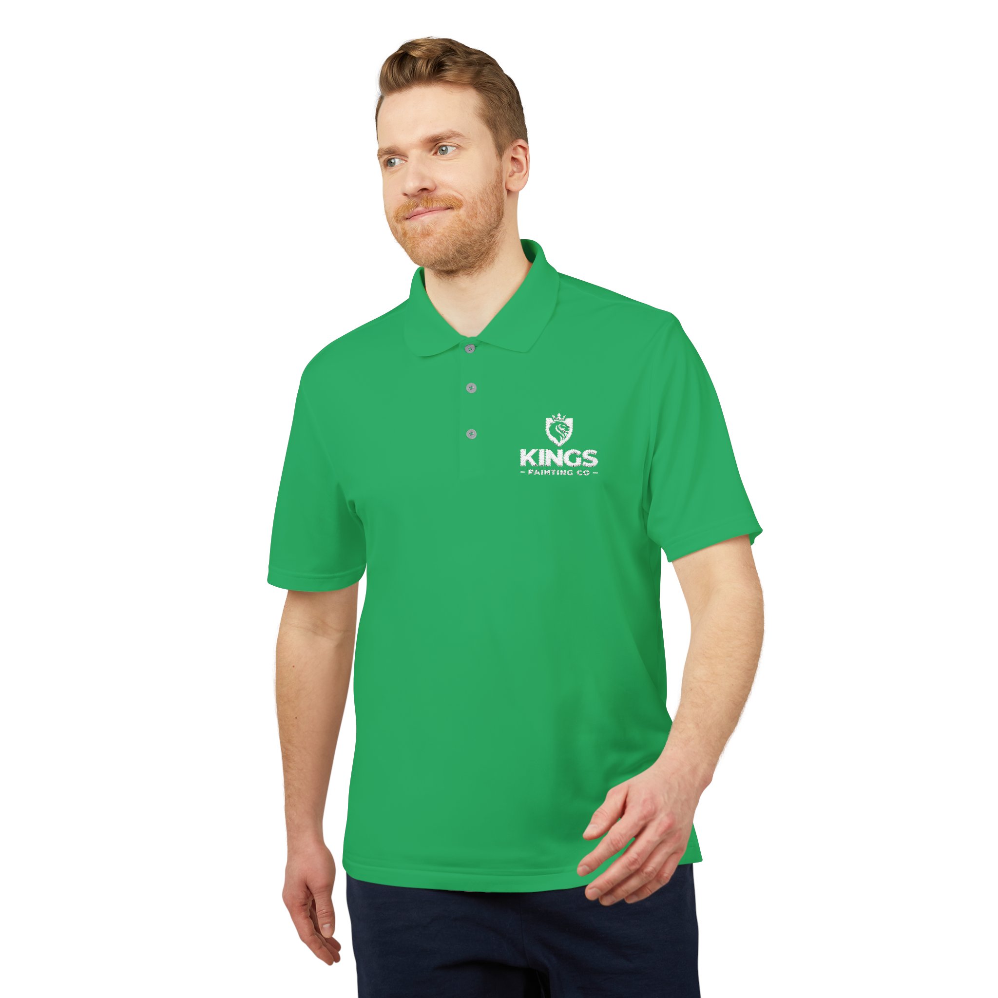 A man with light hair and a beard models the Kings Painting Co. Performance Polo by Under Armour®, featuring a bright green color and a white KINGS logo with crown on the chest. He stands against a white background with a relaxed expression.
